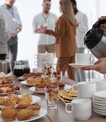 Close up of a continental breakfast at a business conference with blurred attendees wearing lanyards in the background